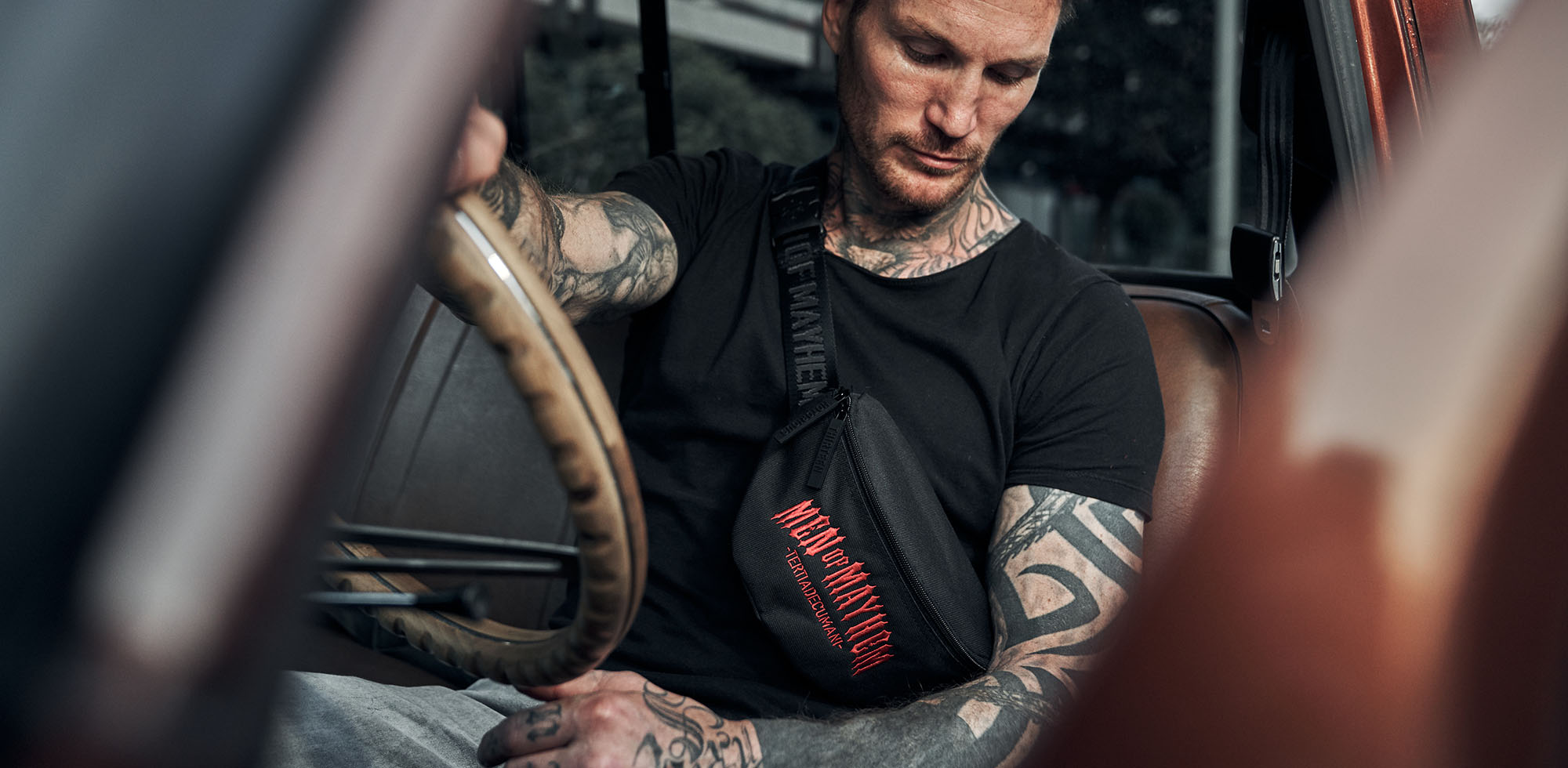 mann sitzend im auto trägt bauchtasche von men of mayhem in schwarz rot