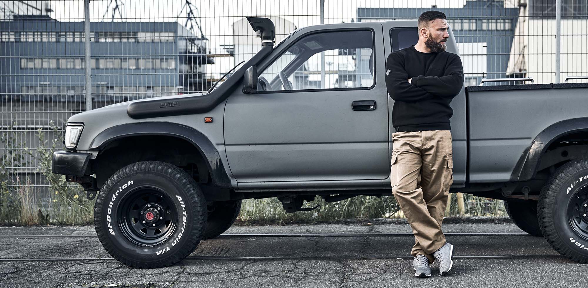 mann stehend vor auto pickup truck und trägt men of mayhem cargo hose in sand in kombination mit men of mayhem crewneck pullover in schwar