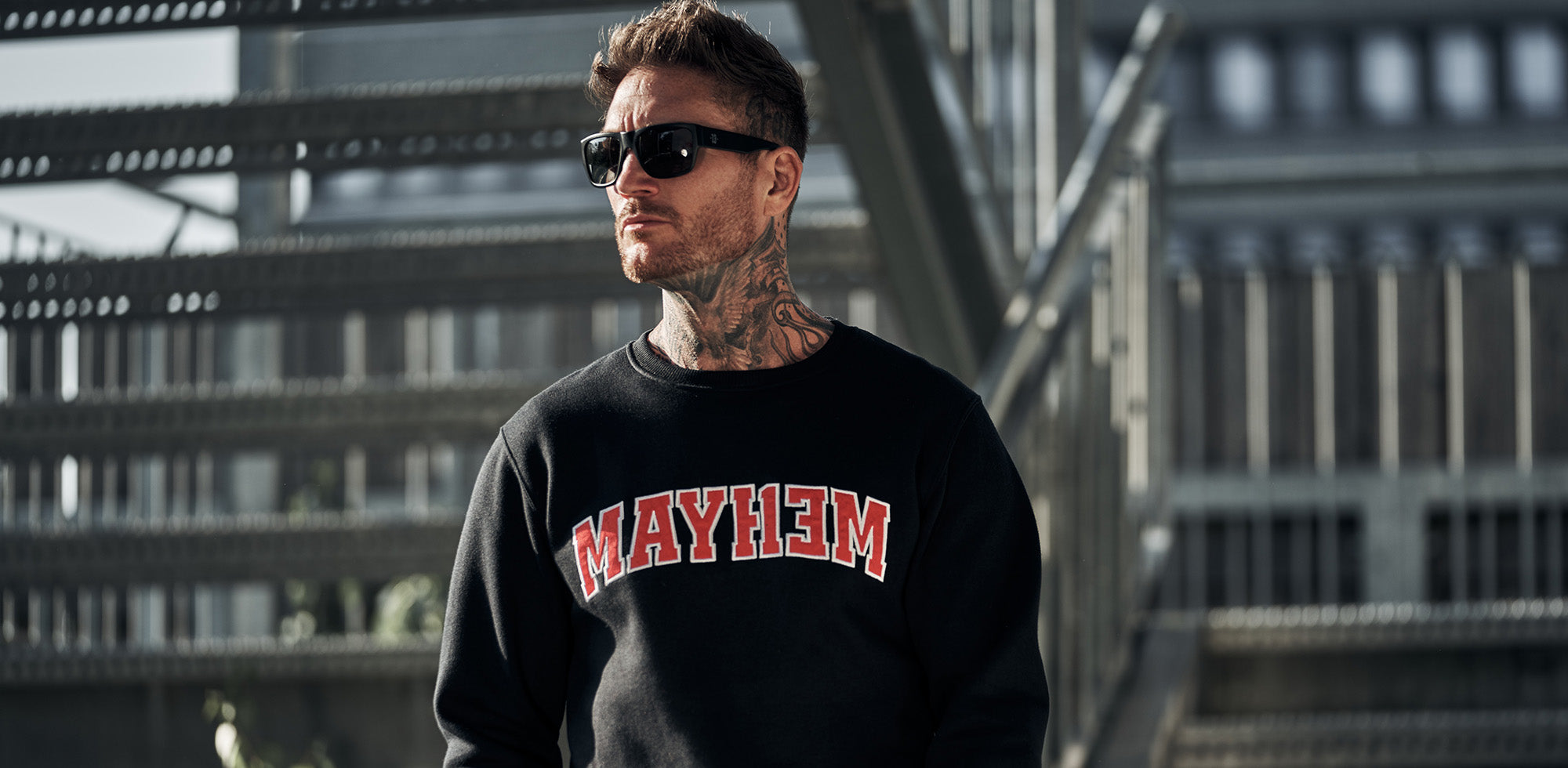 mann stehend vor gebäude trägt men of mayhem league crewneck in schwarz rot weiss und dazu sonnenbrille in schwarz