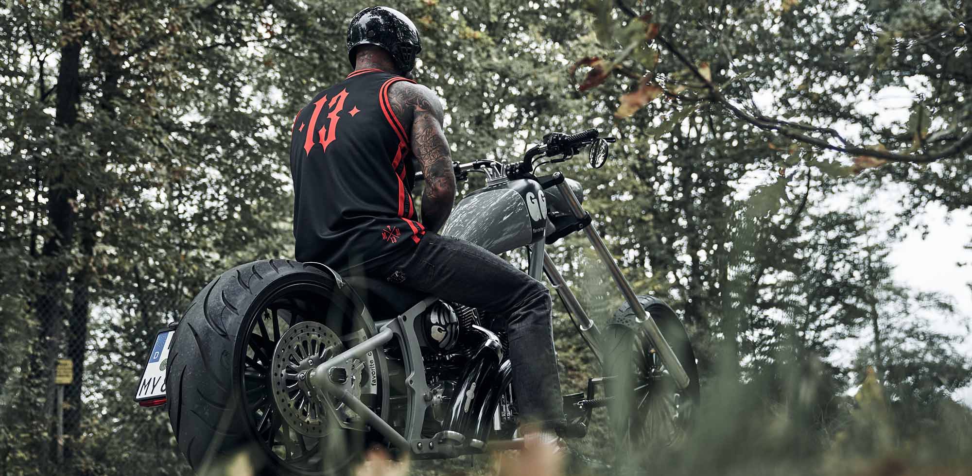 mann istzend auf custom harley davidson trägt men of mayhem mesh tank top in schwrz mit rotem logo auf der brust und große 13 auf dem rücken