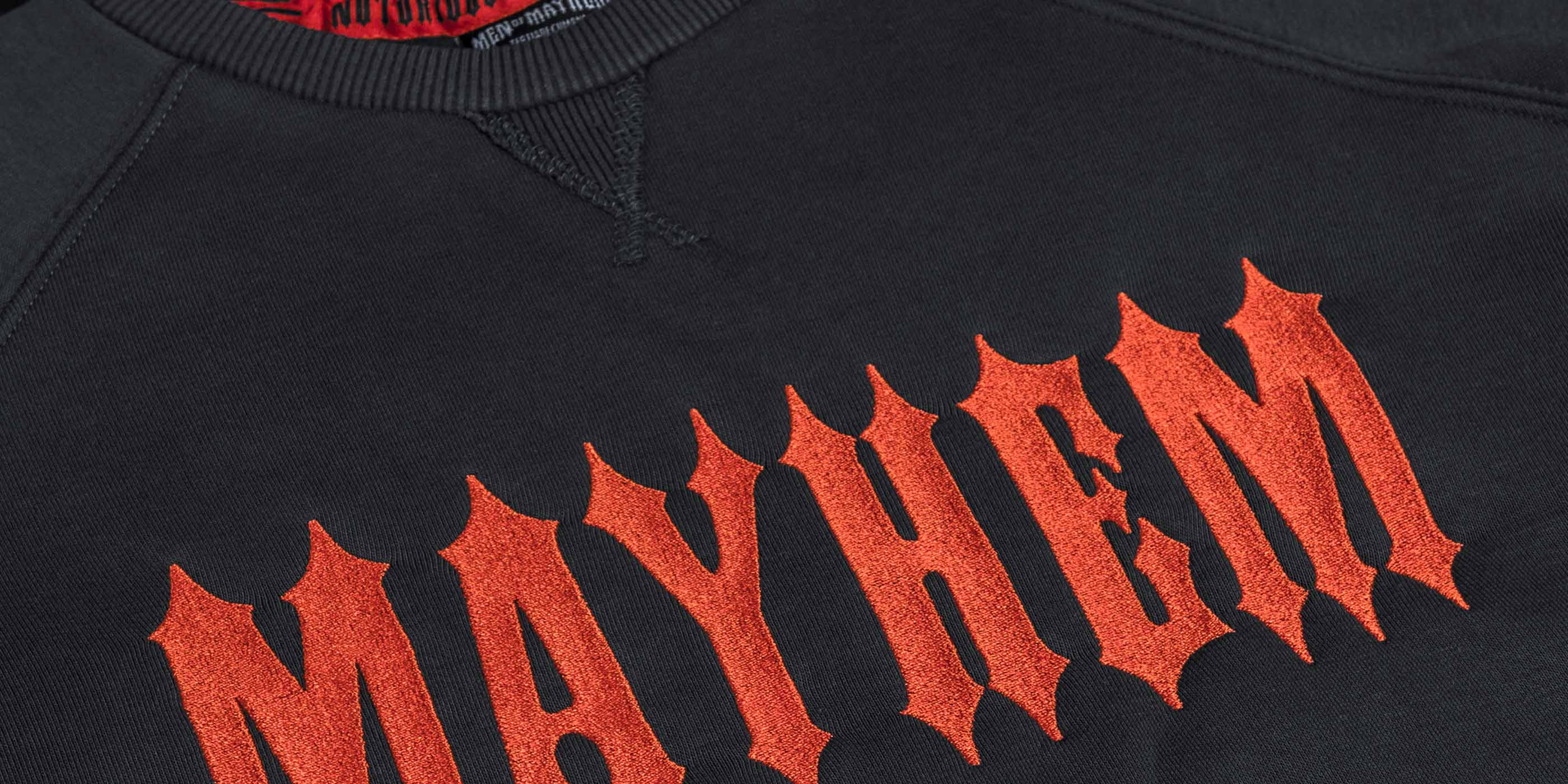 nahaufnahme von einem men of mayhem women crewneck in grau mit orange farbenem stick auf der brust