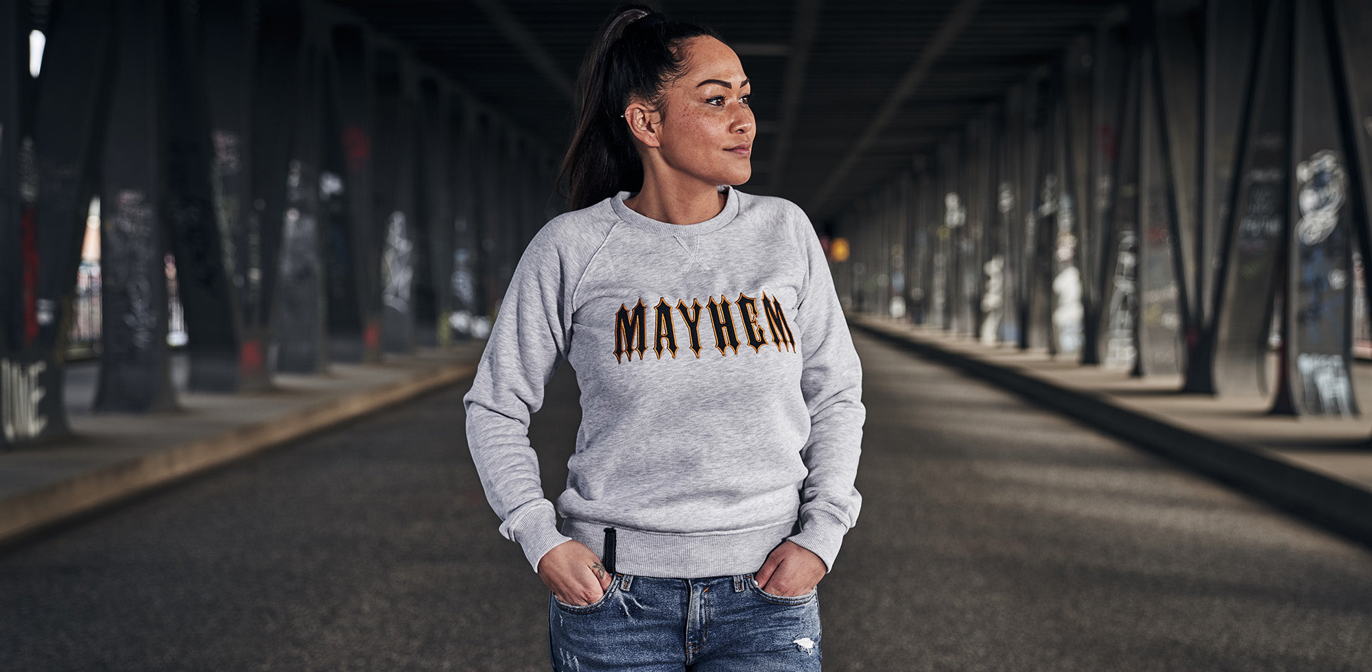 frau stehend auf einer brücke trägt men of mayhem women crewneck in grau