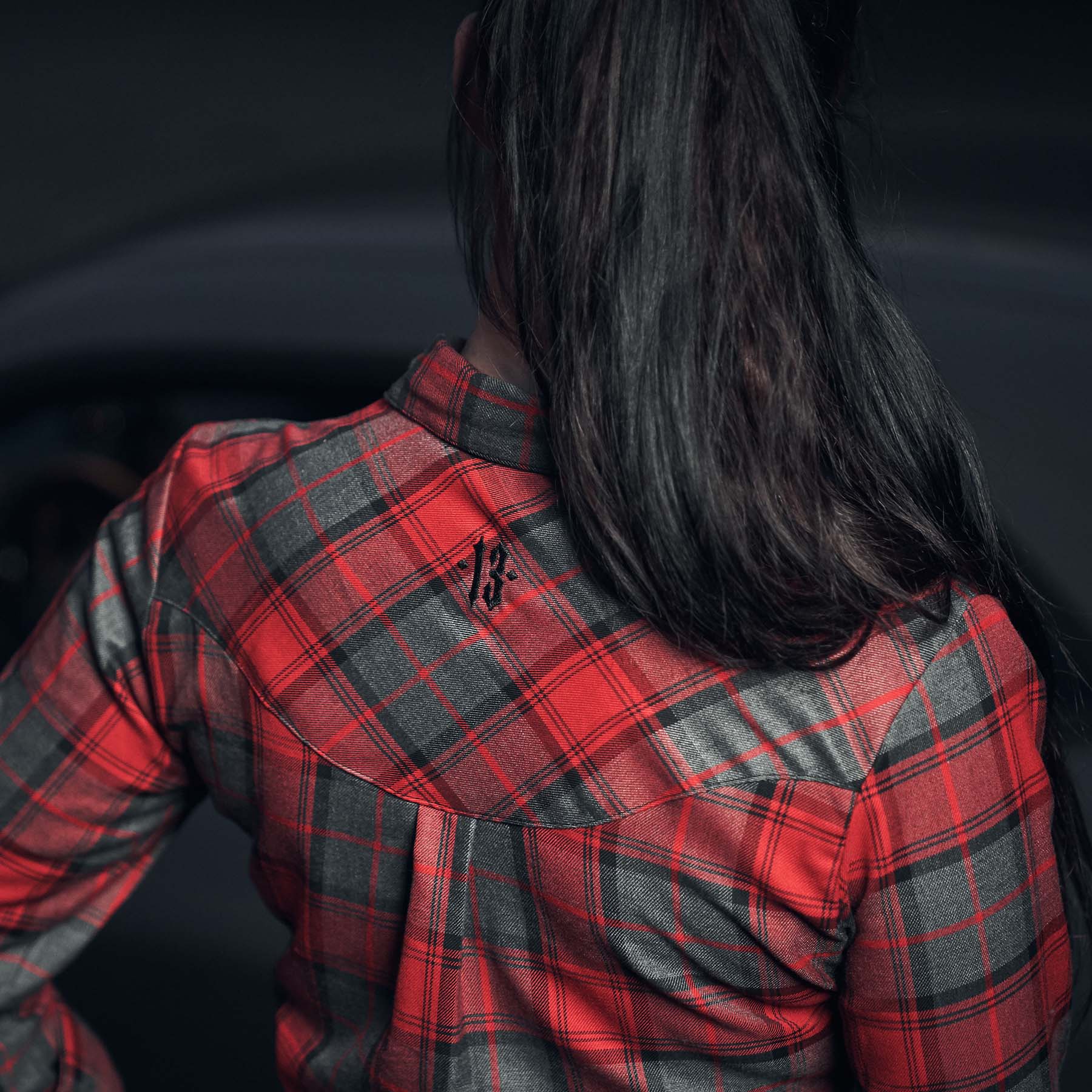frau von hinten mit schwarzem zopf trägt men of mayhem flannelhemd in rot - grau