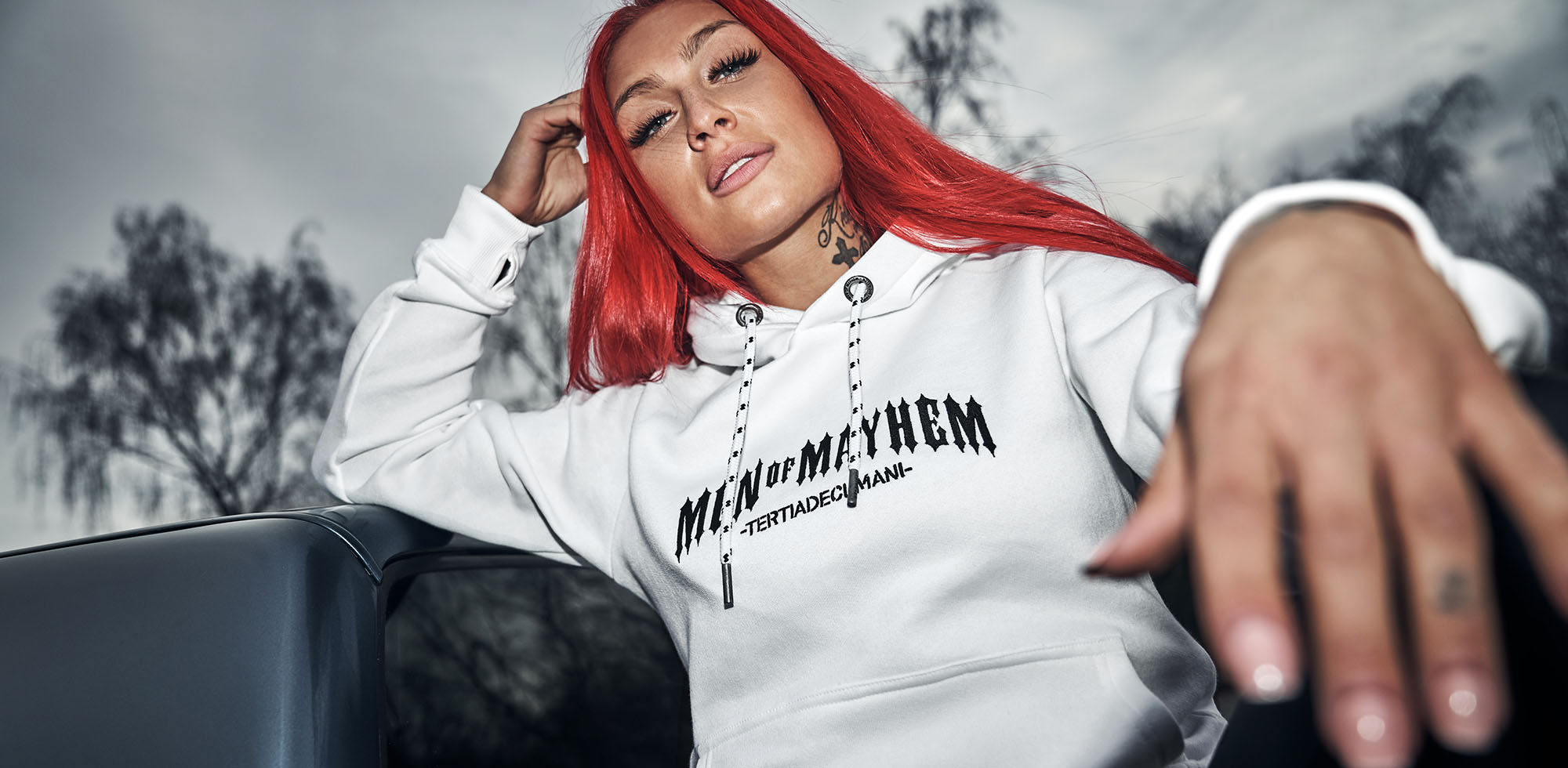 frau mit roten haaren trägt men of mayhem women classic hoody in weiss mit schwarzem logo stick auf der brust
