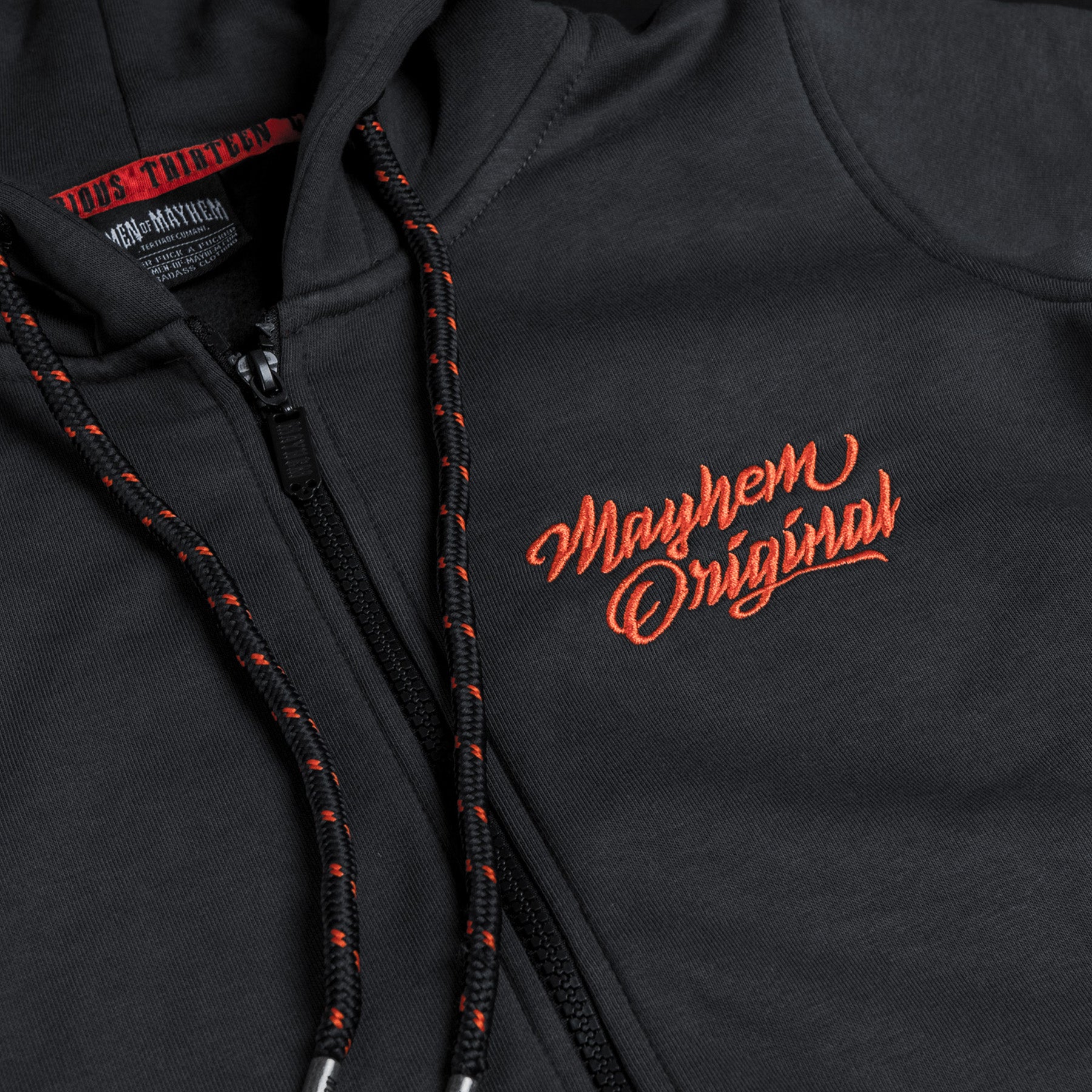 Nahaufnahme eines men of mayhem women zippers modell twof in grau mit orange farbenem stick auf der brust, kapuze und rücken