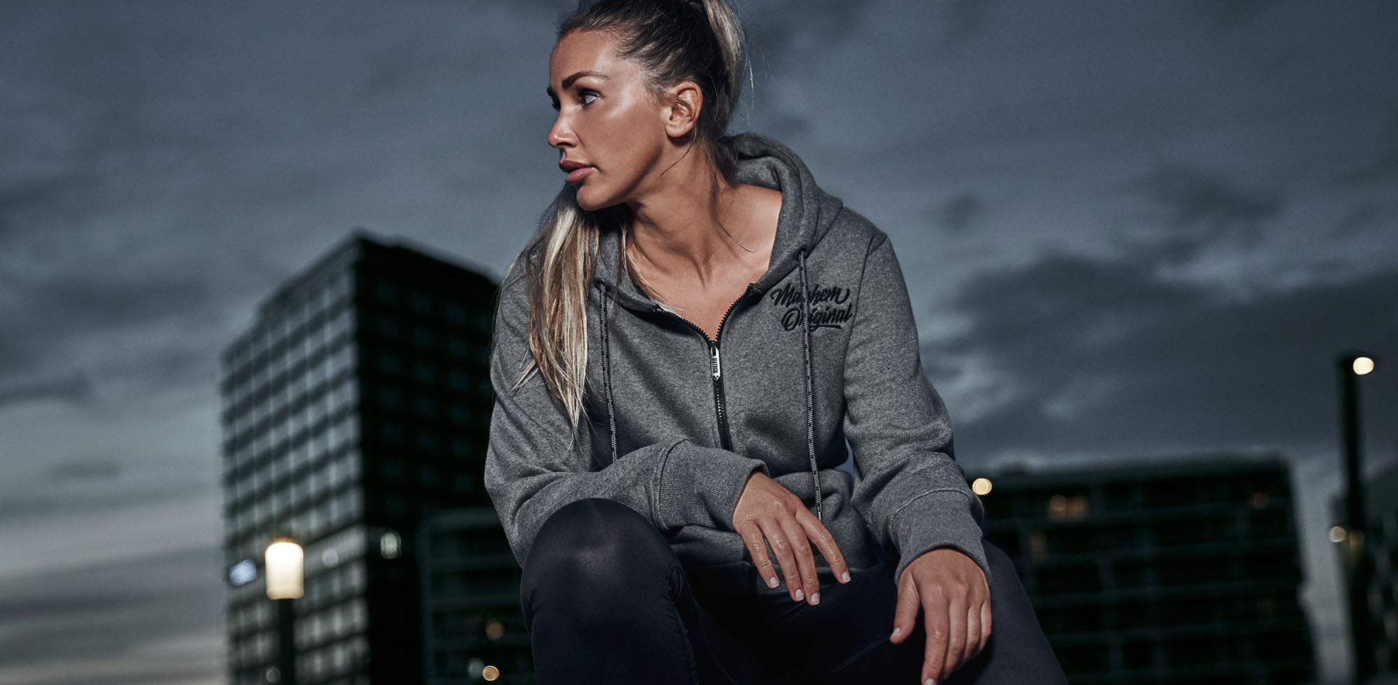 blonde frau sitzend bei dämmerung trägt men of mayhem women zipper twof in grau schwarz mit stick