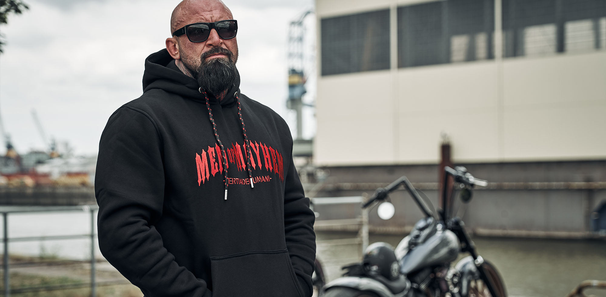 mann mit glatze und bart stehend vor harley davidson am hamburger hafen trägt men of mayhem hoody in schwarz rot - motiv ist gestickt
