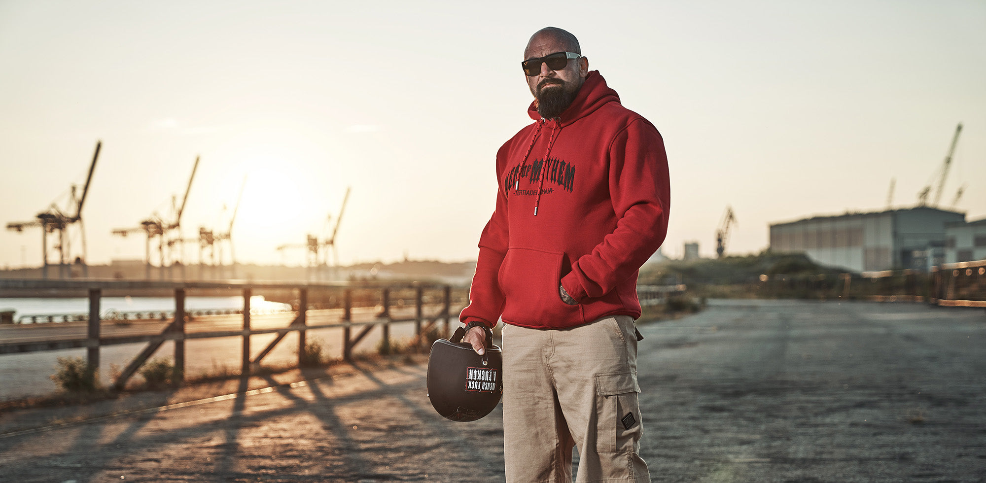 mann stehend am hamburger hafen hält helm in der hand und trägt roten men of mayhem hoody classic 