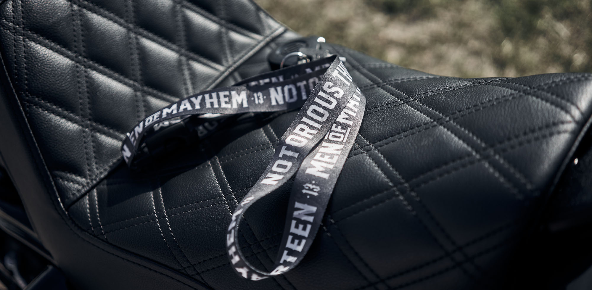 men of mayhem lanyard in dunklem camo mit weißer aufschrift notorious thirteen ligend auf motorrad sitzbank