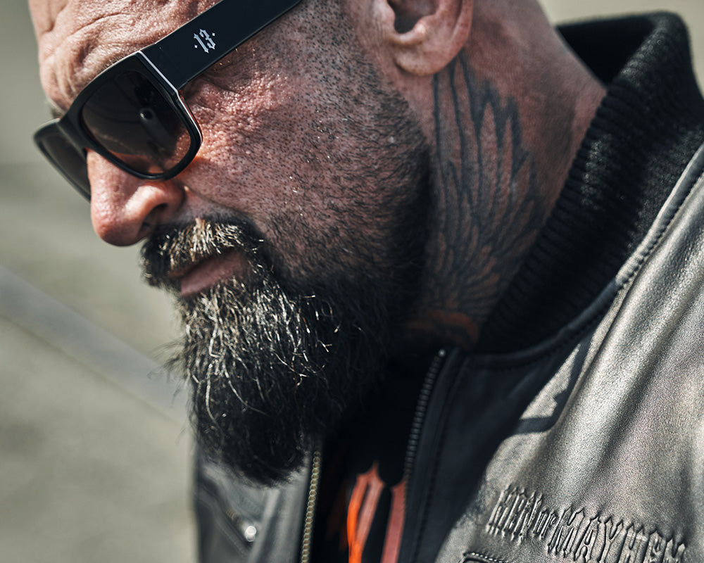 nahaufnahme von einem mann mit tattoo trägt men of mayhem sonnenbrille und lederjacke in schwarz