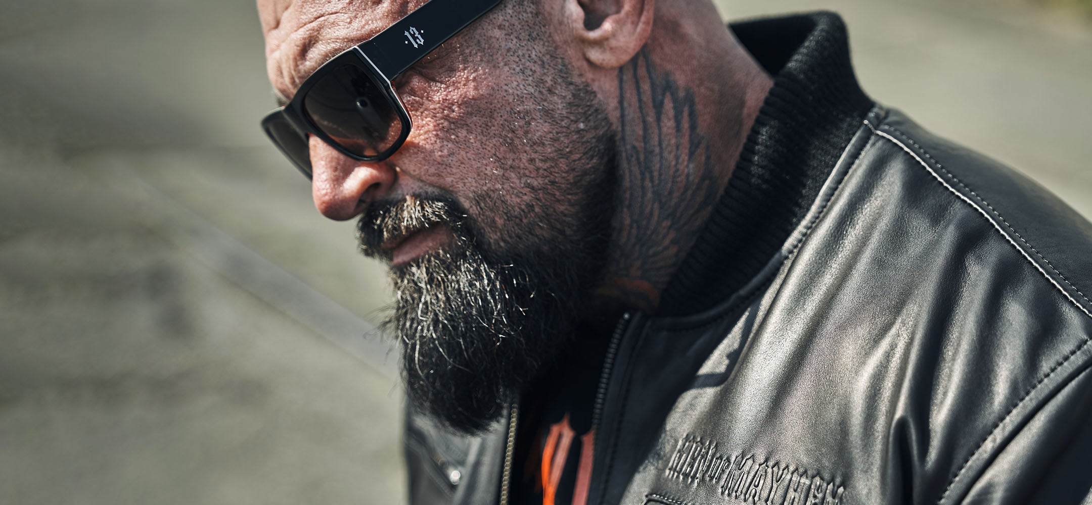 nahaufnahme von einem mann mit tattoo trägt men of mayhem sonnenbrille und lederjacke in schwarz