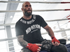 mann mit glatze sitzt im boxring mit bandagierten händen und trägt men of mayhem fight team t-shirt in schwarz mit weißem druck