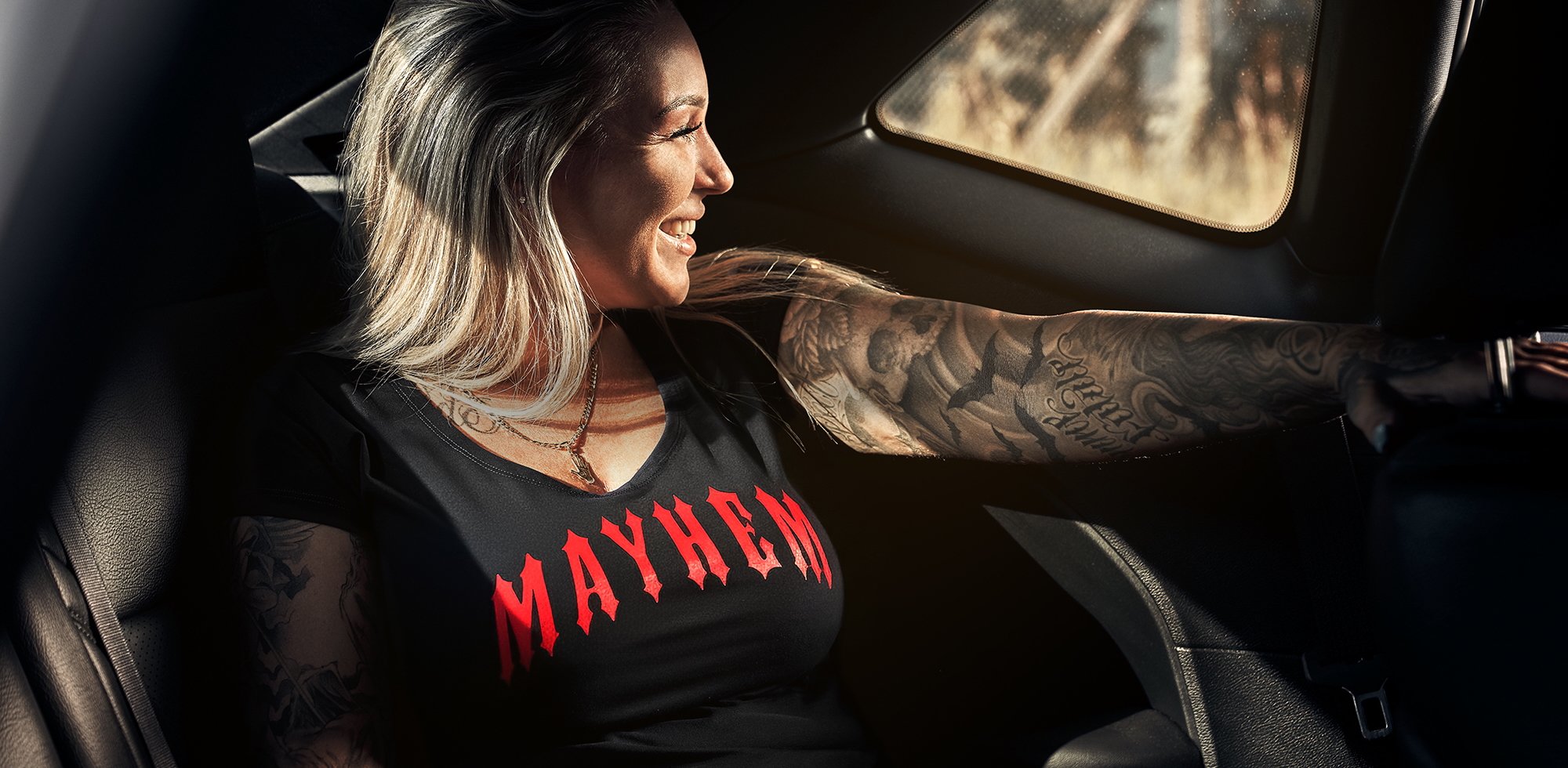 Motorrad-Style Damenbekleidung: Frau im Mayhem T-Shirt am Steuer mit Biker-Tattoos